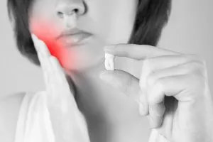 Woman holding a pill and cheek in pain